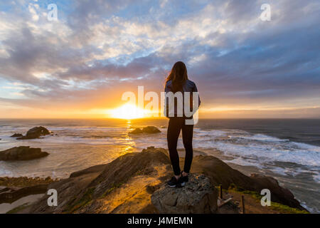 Caucasian woman standing on rock near ocean at sunset Stock Photo