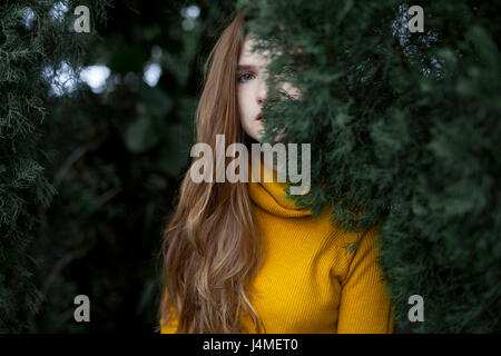 Serious Caucasian woman hiding behind tree Stock Photo