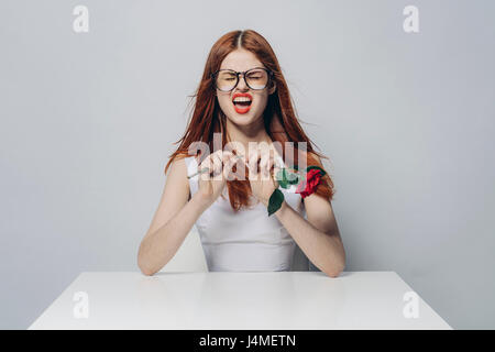 Caucasian woman sitting at windy table snapping stem of rose Stock Photo