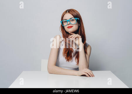 Pensive Caucasian woman sitting at table wearing blue eyeglasses Stock Photo