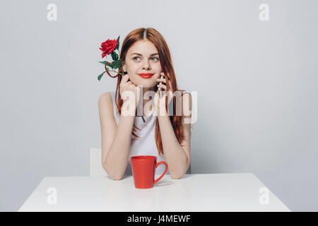 Caucasian woman sitting at table holding rose talking on cell phone Stock Photo