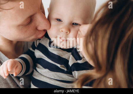 Caucasian mother and father kissing baby son on cheek