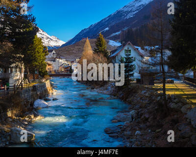 icy river running through village of Andermatt switzerland with snow mountains in background Stock Photo
