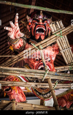 Evil looking red Ogoh-Ogoh being prepared for the Ngrupuk Parade on the eve of Balinese New Year. Scary heads in stomach, knees and fierce face Stock Photo