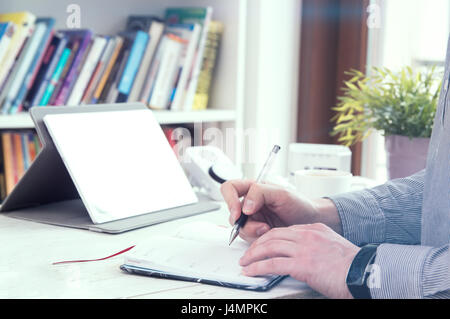 Man fills his planner and a tablet on background with empty space for your text. Stock Photo