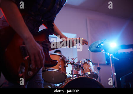 Mid-section portrait of unrecognizable musician playing guitar on stage of urban club, during gig, focus on guitar strings in dim lighting Stock Photo