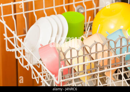 Close-up picture of opened dishwasher with clean plates and colored bowls on its rack Stock Photo