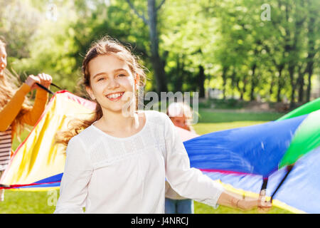 Close-up portrait of happy Caucasian girl waving colorful parachute with her friends outdoor in spring Stock Photo