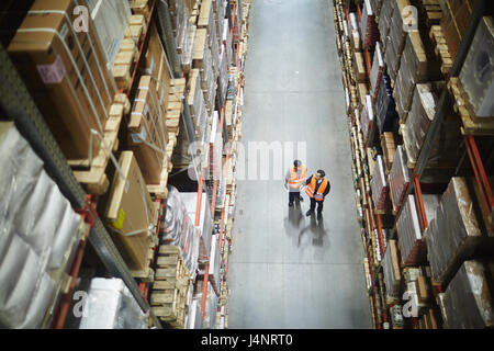 Two men in uniform standing in aisle between large-scale shelves and talking Stock Photo