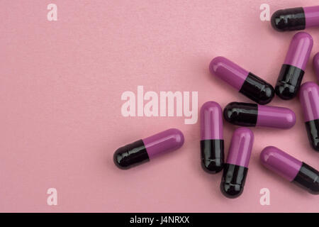 Many medicines purple and black pills capsules on pink background Stock Photo