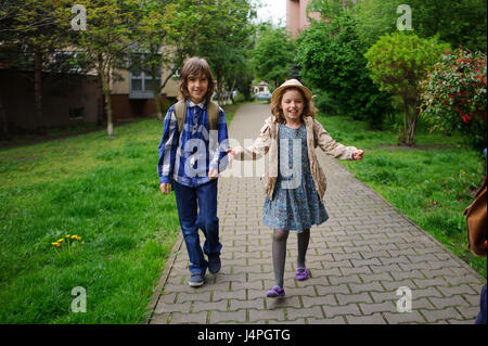 Elementary school students hurry to school. Schoolboy and schoolgirl with backpacks behind the back go to the lesson. Stock Photo