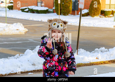 Little girl shoveling snow on home drive way. Child with shovel playing outdoors in winter season. Stock Photo