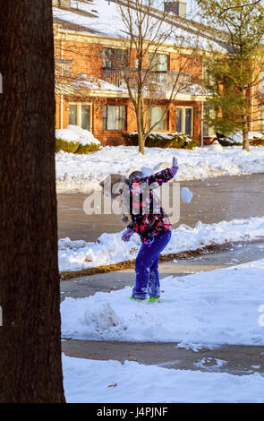 Little girl shoveling snow on home drive way. Child with shovel playing outdoors in winter season. Stock Photo