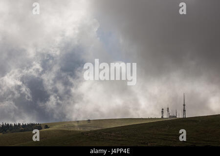 Some antennas on top of a mountain with a wall of clouds and fog Stock Photo