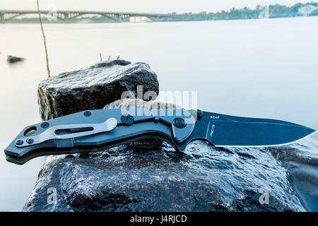 Holder knife on stone. River. City. Pocket knife. Stock Photo