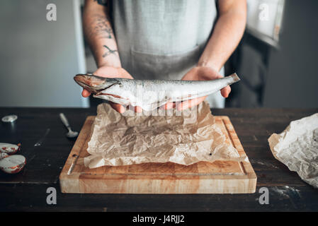 Male chef hands holds raw fish over wooden cutting board. Seafood cooking. Fresh sea food Stock Photo