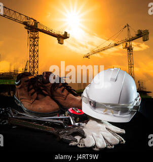 helmet and construction equipment with building and crane against dusky sky use for construction business theme Stock Photo