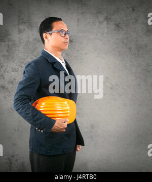 portrait of self conficence engineering man holding safety helmet against cement wall Stock Photo