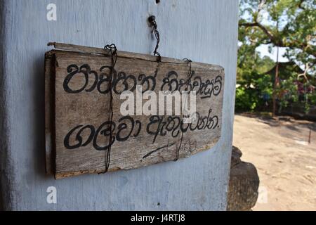 A hand written notice, on a wooden plank at the entrance to the Gadaldeniya Temple reads,'Please remove your shoes and headdresses before entering' Stock Photo