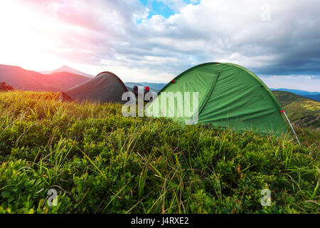 A couple of tourist sitting near they tent against the backdrop of an incredible mountain landscape. Orange sunset glowing by sunlight Stock Photo