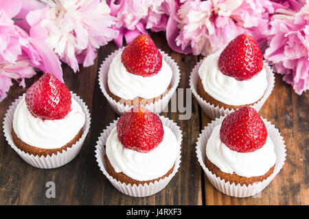 Cupcakes with Strawberries Decorated with Pink Peonies. Stock Photo