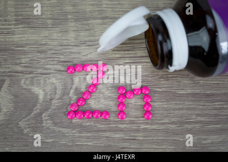 Pink pills forming shape to Zn alphabet on wood background Stock Photo