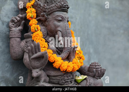 Ganesha with balinese Barong masks sitting on front of temple. Decorated for religious festival by orange flowers necklace and ceremonial offering. Tr Stock Photo