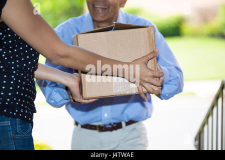 Closeup portrait of delivery man handing package to woman inside house, isolated outdoors background Stock Photo