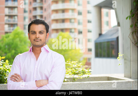 Closeup portrait, happy handsome man in pink shirt, arms folded, crossed, standing outside of his office during sunny day, isolated balcony background Stock Photo