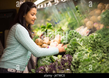 Closeup portrait, beautiful, pretty young woman in sweater picking up, choosing green leafy vegetables in grocery store Stock Photo