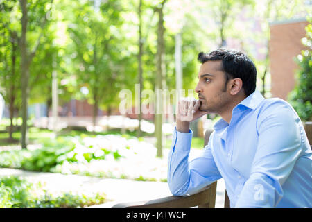 Closeup portrait, stressed young business man, hand on head, worried, isolated background of trees outside. Negative human emotion facial expression f Stock Photo