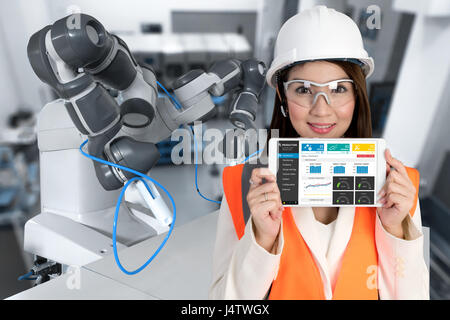 Smile young Asia female Engineer using tablet , wear glasses , automation robot arm machine in smart factory industrial with tablet real time monitori Stock Photo