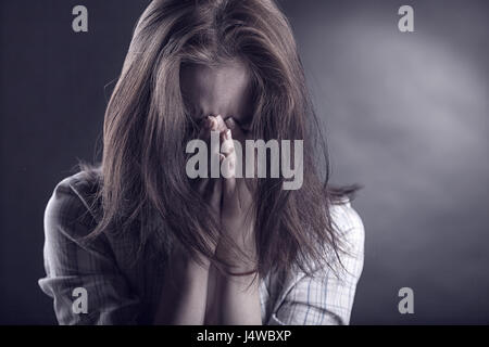 Young woman crying face in her hands on a dark background Stock Photo