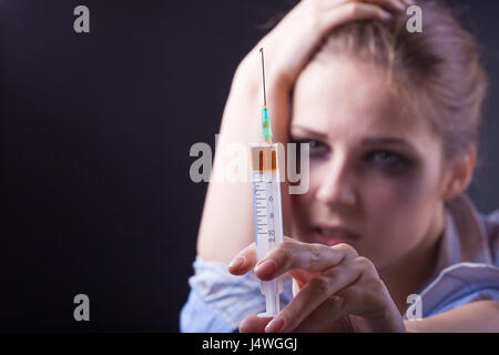 Young woman with drug addiction on dark backgroundю Focus on syringe Stock Photo