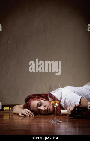 Drunken young woman lying on the floor. Focus on glass Stock Photo