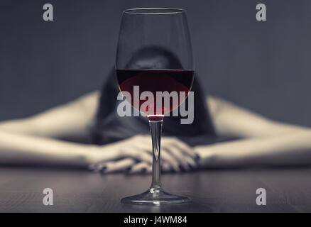 Woman in depression, drinking alcohol on dark background. Focus on the glass Stock Photo