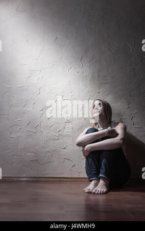 Young sad woman sitting alone on the floor in an empty room Stock Photo