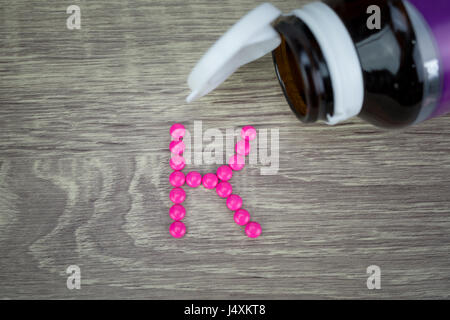 Pink pills forming shape to K alphabet on wood background Stock Photo