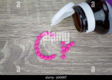 Pink pills forming shape to Cr alphabet on wood background Stock Photo