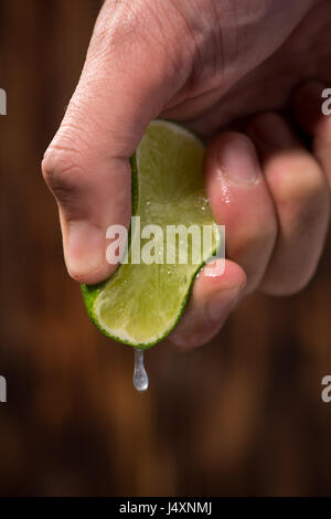 Hand squeeze lime with lime drop on dark wooden background Stock Photo