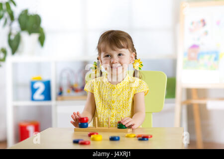 Kid girl playing with logical toy on desk in nursery room or kindergarten. Child arranging and sorting colors and sizes Stock Photo