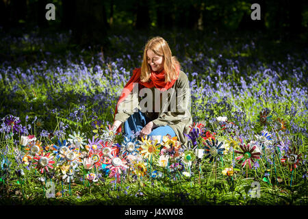 Designer Lottie Hanson-Lowe arranges flowers made with recycled litter by artist Michelle Reader, sits among dozens planted on the forest floor as part of an art installation in the Forest of Dean, Gloucestershire, to raise awareness of rural litter problems in the area. Stock Photo