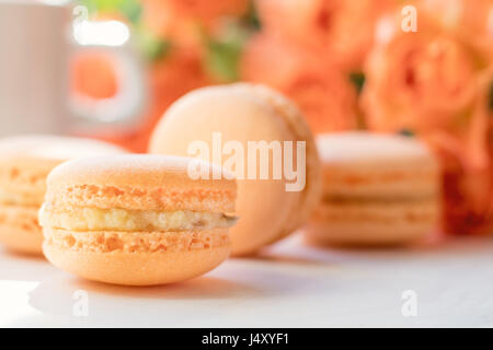 Orange mango or citrous macaroons and orange fresh little roses on light wooden background. Coloring and processing photo with light vintage style. To Stock Photo