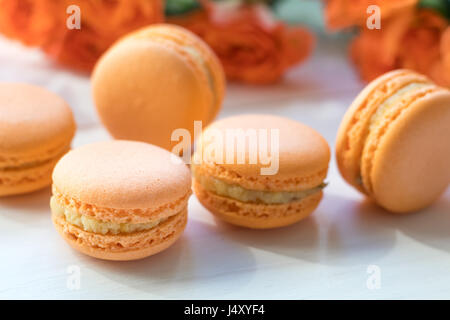 Orange mango or citrous macaroons and orange fresh little roses on light wooden background. Coloring and processing photo with light vintage style. To Stock Photo