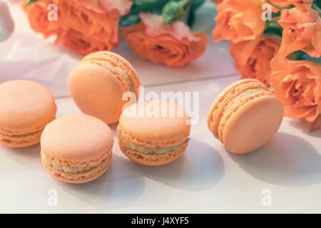 Orange mango or citrous macaroons and orange fresh little roses on light wooden background. Coloring and processing photo with light vintage style. To Stock Photo