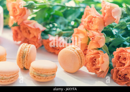 Orange mango or citrous macaroons and orange fresh little roses on light wooden background. Coloring and processing photo with light vintage style. To Stock Photo