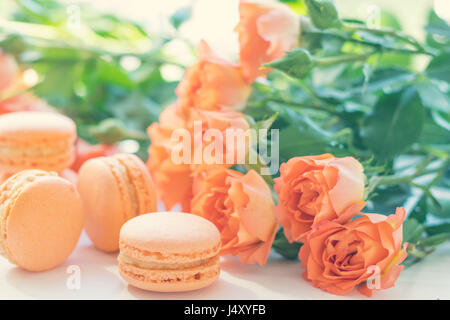 Orange mango or citrous macaroons and orange fresh little roses on light wooden background. Coloring and processing photo with light vintage style. To Stock Photo