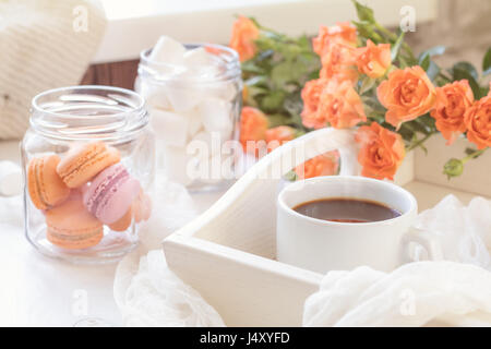 Orange mango macaroons, cup of coffee, marshmallow and fresh little roses on light wooden background. Sunlight. Coloring and processing photo with lig Stock Photo