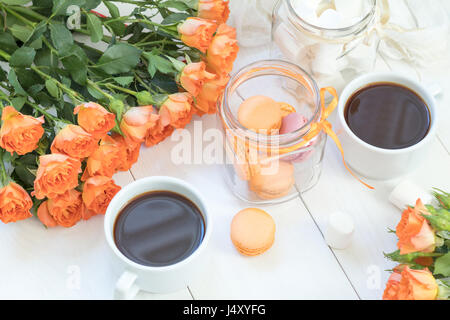 Orange mango macaroons, cup of coffee, marshmallow and fresh little roses on light wooden background. Sunlight. Coloring and processing photo with lig Stock Photo