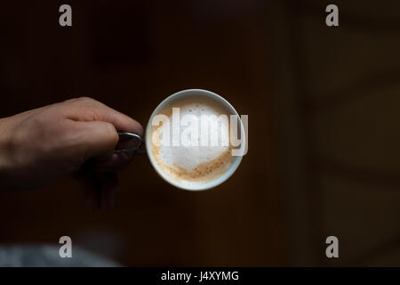 Coffee espresso cup with milk in hand on dark blurry background. Man holding mug. Stock Photo